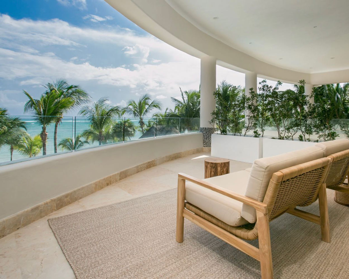 A shaded terrace with lounge chairs looking out over the palms to the sea
